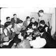 Y.M.-Y.W.H.A. boys' club, Brunswick Avenue, [ca. 1950]. Ontario Jewish Archives, Blankenstein Family Heritage Centre, fonds 61, series 6, item 25.|This item is a glass slide of a group of members of a Y.M.-Y.W.H.A. boys' club having a discussion while sitting around a table. There is Hebrew writing on the chalkboard behind them.